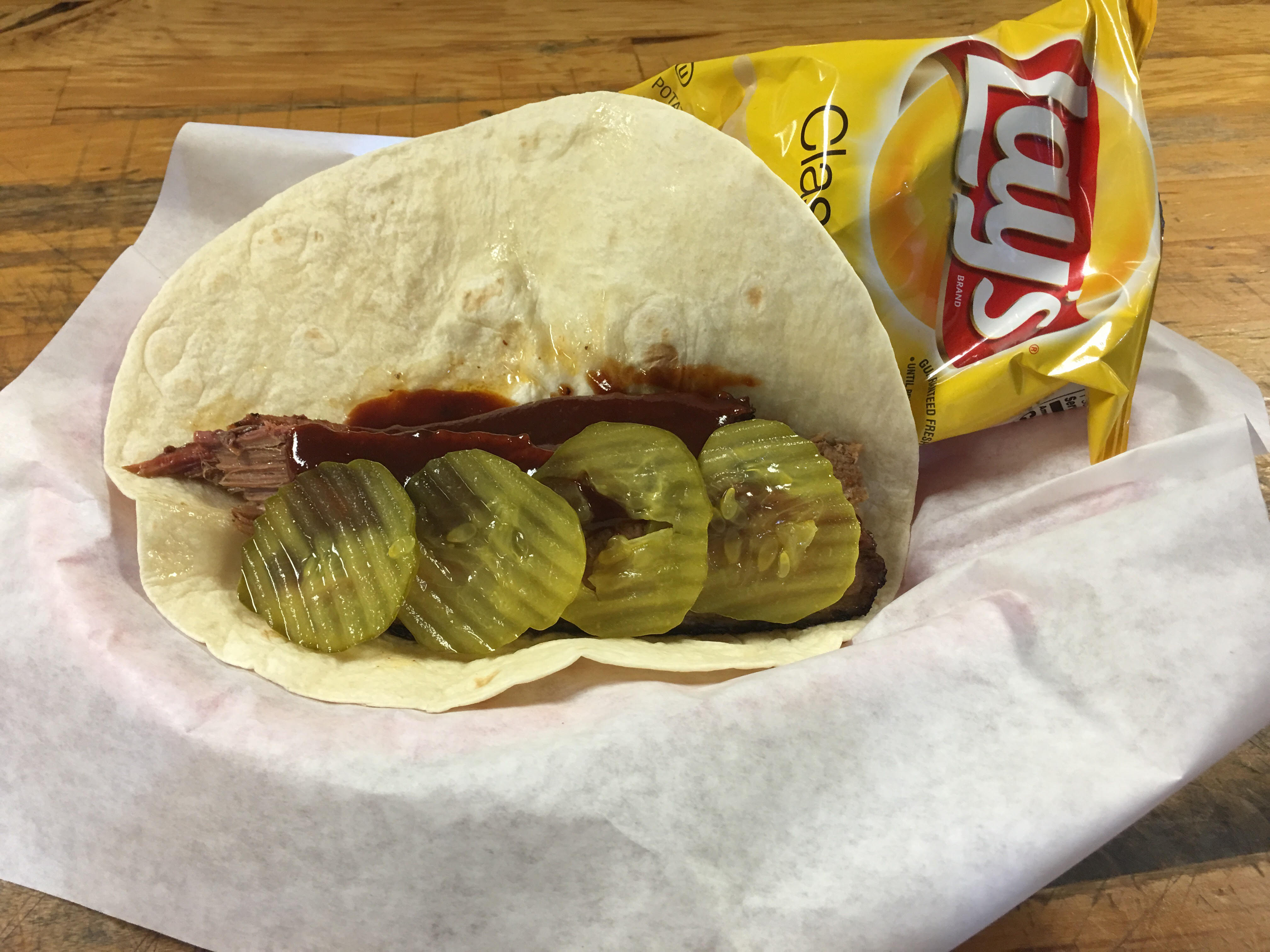 Sliced brisket wrapped in a flour tortilla with pickles, ready for takeout at R & R BBQ